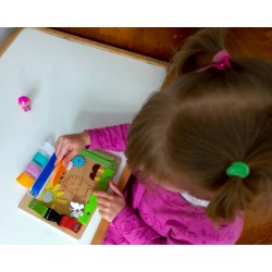 Dziewczynka w różowej bluzce bawi się tablicą manipulacyjną, patrząc na jeżyka pod pomarańczowym okienkiem.