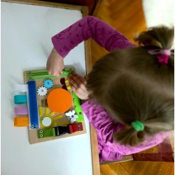Dziewczynka otwierająca zielony zamek błyskawiczny na kolorowej mini tablicy manipulacyjnej.