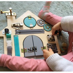 Dziecko bawiące się tablicą manipulacyjną w kształcie domku o miętowo szarych elementach